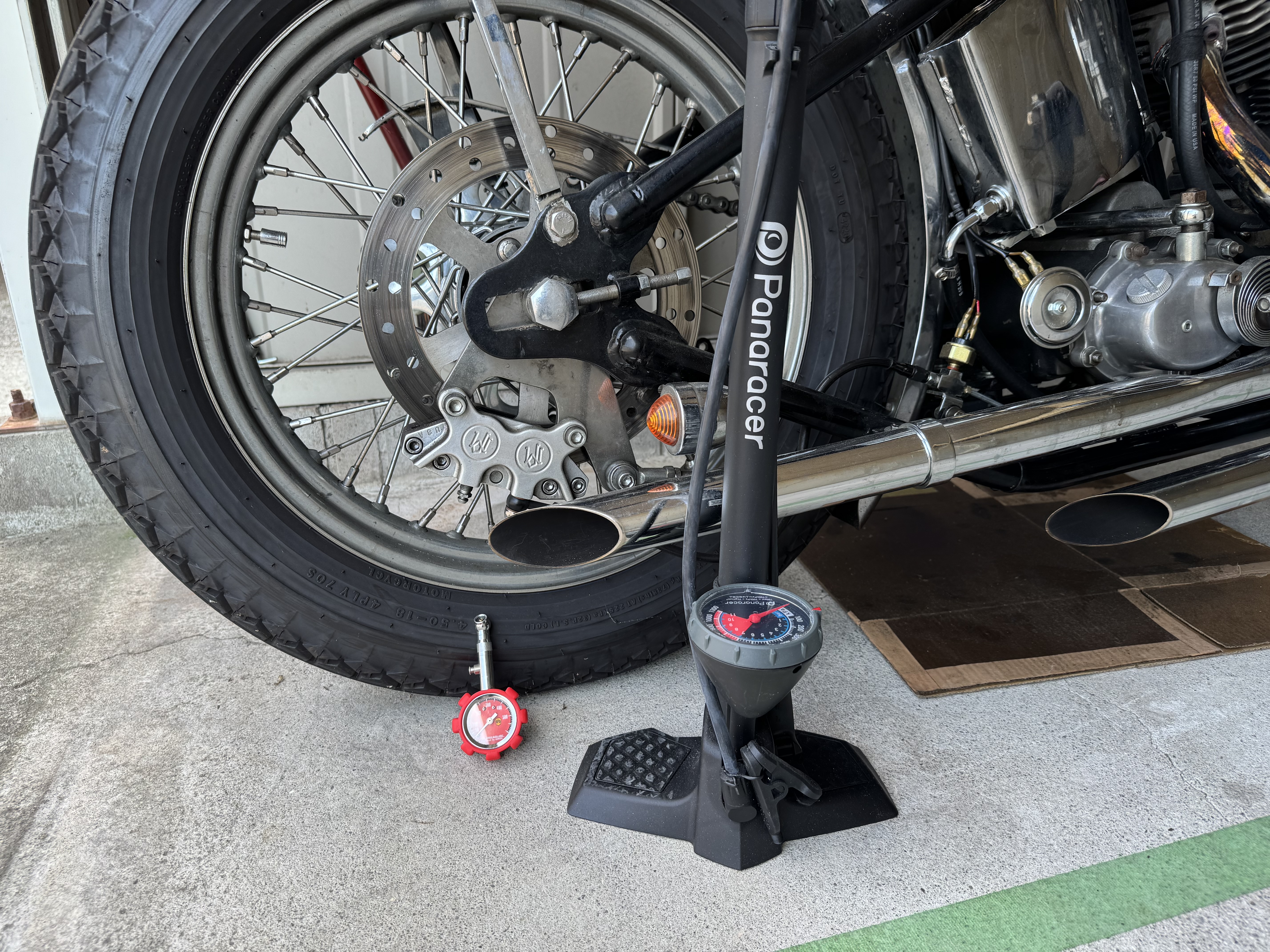 ショベルヘッドのバイクタイヤをエアゲージと自転車ポンプで空気圧調整中の様子