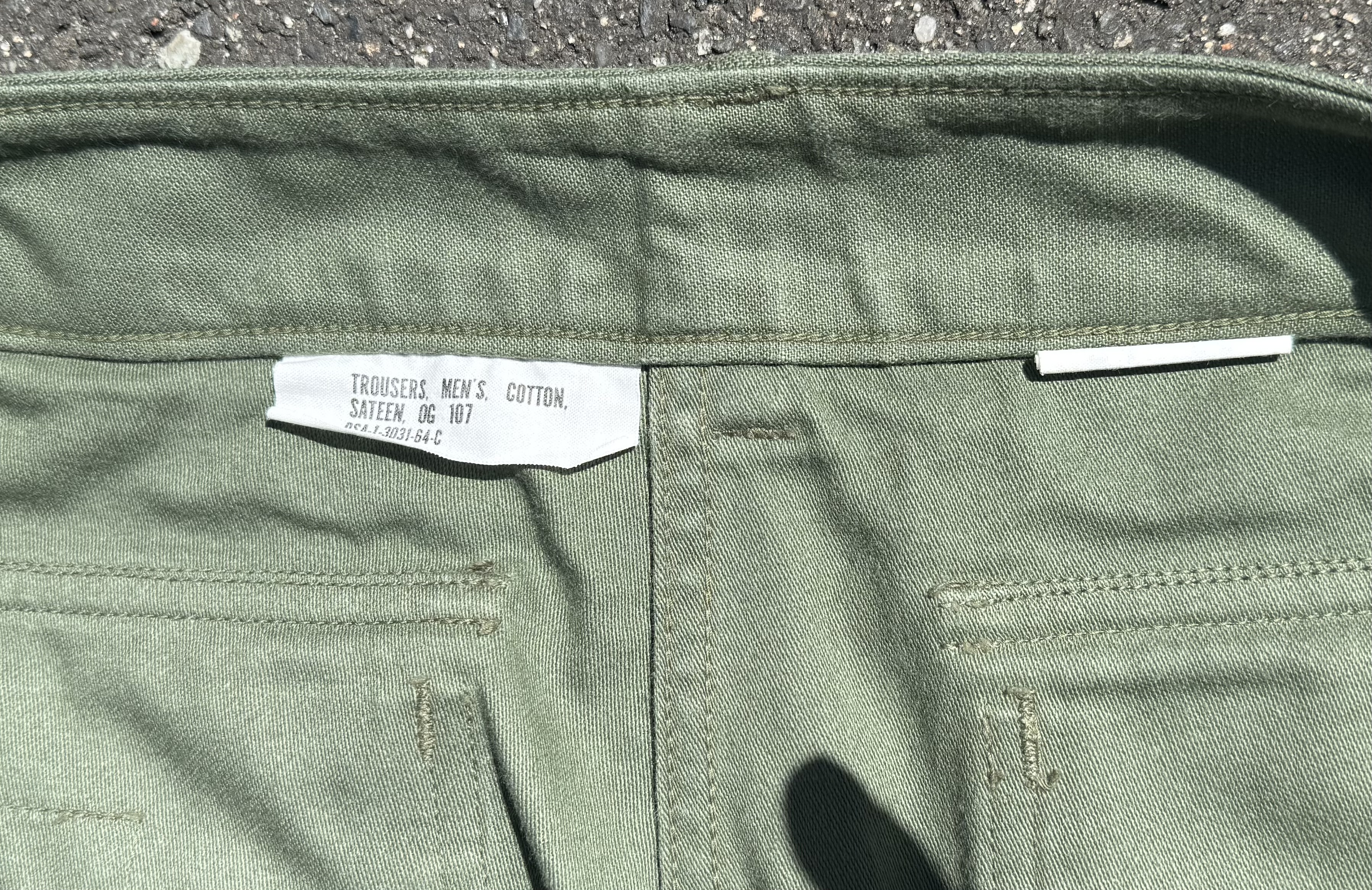 ベイカーパンツの内側にあるミルスペックタグのアップ。「TROUSERS, MEN'S, COTTON, SATEEN, OG-107」の文字が記されている。